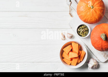 Ansicht von Kürbis Stücke in der Schüssel, Kürbiskerne und Knoblauch auf Tisch Stockfoto