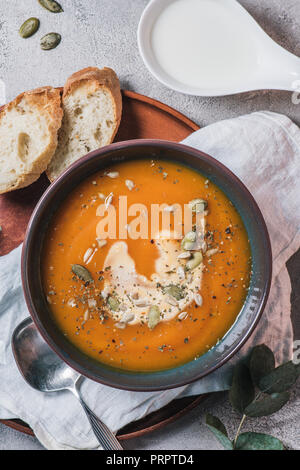 Ansicht von Kürbis Cremesuppe mit Samen in der Schüssel und Brot auf Holzbrett auf Tisch Stockfoto