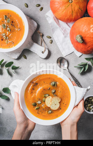 7/8 Bild der Frau hält Teller mit hausgemachten Kürbis Cremesuppe mit Samen und Zwieback auf Tisch Stockfoto