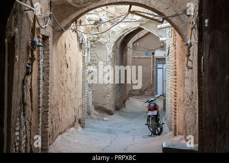 YAZD, IRAN - August 9, 2018: Motorcycyle in eine typische Straße der Altstadt von Yazd, Iran, mit seinen typischen Lehm Wände und Gebäude. Yazd ist Stockfoto