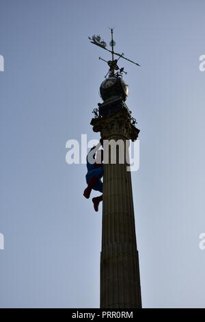 Superhelden Klettern ein Obelisk mit Uhr und Windfahne. Blue Sky Hintergrundbeleuchtung. Stockfoto