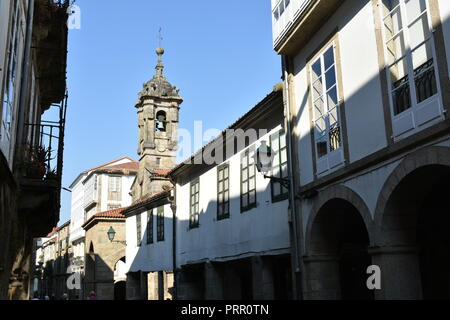 Straße mit weißen Wänden, Lichter, grünen und weißen Fenstern und den Kirchturm. Santiago de Compostela, Spanien. Stockfoto