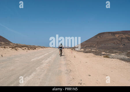 Lanzarote, Kanarische Inseln: junge Radfahren auf dem Schmutz der Straße zum Strand Playa de Las Conchas im Norden von La Graciosa, die Inselgruppe Chinijo Inseln Stockfoto