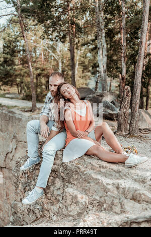Curly Frau in Kleid und weißen Turnschuhen in der Nähe ihrer schönen Mann sitzen Stockfoto