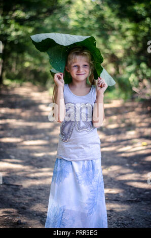 Schöne kaukasische Mädchen mit grünem Klette Anlage im grünen Wald Stockfoto