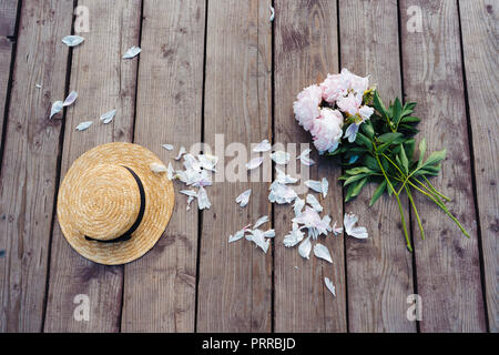 Auf einer hölzernen Pier liegt, hat eine Frau und einen Strauß Pfingstrosen. Stockfoto