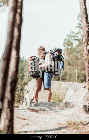 Zarte Frau mit schweren Rucksack umarmte ihre starken Mann bärtigen beim Wandern Stockfoto