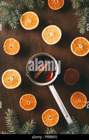 Blick von oben auf die heißen Glühwein im Topf mit frischen Orangen auf hölzernen Hintergrund Stockfoto