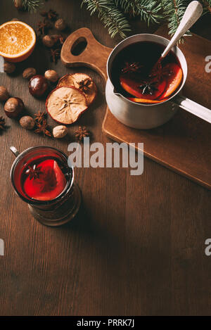 Heißer Glühwein in Kochtopf und Glas Schale mit Gewürzen auf hölzernen Hintergrund Stockfoto