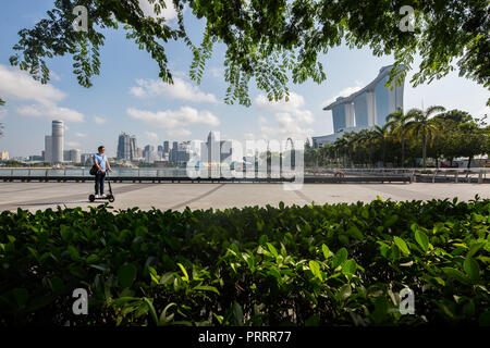 Durch das Laub, um einen Mann auf seiner Beweglichkeit zu sehen Scooter fahren vorbei an der Kulisse von Singapur ikonischen Blick Stockfoto