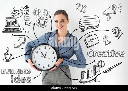 Lächelnd Geschäftsfrau holding Wanduhr in Händen von Weiß mit kreativen Geschäftsidee Inschrift und handgezeichneten Symbole Stockfoto