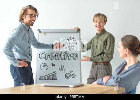 Lachend Geschäftsleute zeigen kreative Inschrift und die Zeichen auf flipchat zu Geschäftsfrau Stockfoto