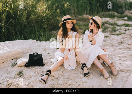 Elegante junge Frauen mit Tassen Kaffee Latte sitzen auf dem Boden Stockfoto