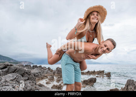 Low Angle View glückliches junges Paar Huckepack auf felsigen Strand in Montenegro Stockfoto