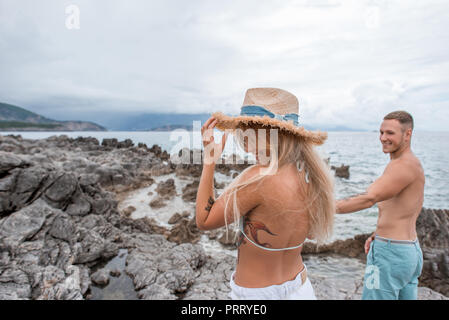 Lächelnden jungen Mann an schöne glückliche junge Frau mit Strohhut auf felsigen Strand in Montenegro Stockfoto