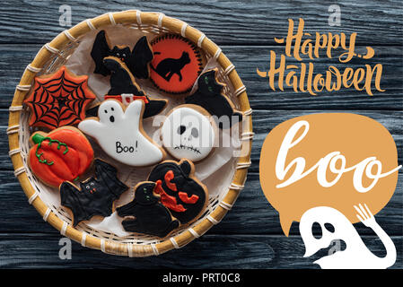 Blick von oben auf die Weidenkorb mit hausgemachten Spooky Halloween Cookies auf Holztisch mit "Happy Halloween" und Ghost mit 'Buh' Schriftzug Stockfoto