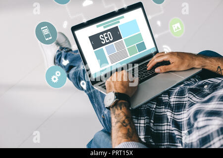 7/8-Ansicht von tätowierten Entwickler arbeiten am Laptop mit SEO Icons Stockfoto