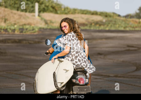 Rückansicht des Paar reiten Roller mit Surfbrett am Strand in Bali, Indonesien Stockfoto