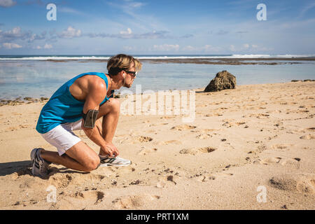 Sportler auf sneakers Schnürsenkel binden am Strand in der Nähe von Meer Stockfoto