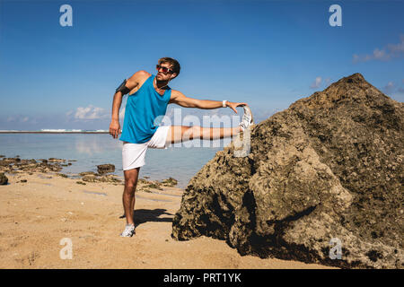 Sportlicher Mann stretching Bein in der Nähe von Felsen am Strand Stockfoto