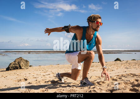 Sportlicher Mann mit Armband tun stürzt während des Trainings am Strand in der Nähe von Meer Stockfoto