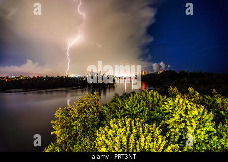 Beleuchtung Streik foto Erfassung während ein Sturm in der Nacht über einen Fluss mit hellen Lichter der Stadt im Hintergrund und Wald Bäume beleuchtet von elektrischen Stockfoto