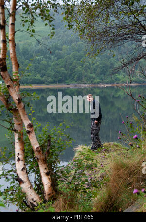 Teenager stehen auf einem Felsen mit Blick auf die ruhigen, reflektierenden Gewässern des Wassers von Kyle von Lochalsh in den schottischen Highlands, Schottland Stockfoto