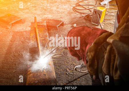 Nahaufnahme von einem Baumeister Schweißer in Braun Arbeitskleidung Schweißnähte ein Metall Produkt mit arc welding Maschine in der Fabrik, eine lose Werkzeuge und constraction Stockfoto