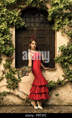 Spanische Frau im roten Kleid vor einem alten Fenster posieren. Stockfoto