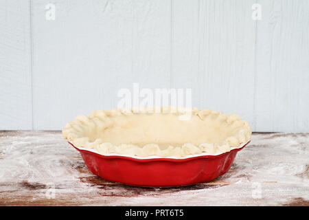 Hausgemachte butter Pie Crust in Pie Platte mit geriffelten Rand eingeklemmt gegen einen rustikalen Holzmöbeln Hintergrund. Kruste ist leer und bereit zum Backen. Stockfoto