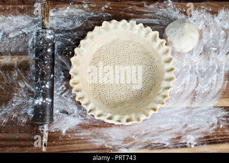 Hausgemachte butter Pie Crust in Pie Platte mit geriffelten Rand gequetscht, nudelholz und extra Ball von Teig über Bemehlten rustikalen Holzmöbeln Hintergrund. Kruste ist Stockfoto