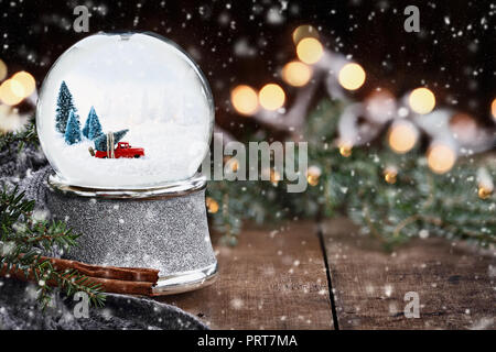 Rustikale Bild einer Schneekugel mit alten Pick up Tuck schleppen einen Weihnachtsbaum von Pinien Zweige, Zimtstangen und eine warme Grau Schal umgeben. Stockfoto