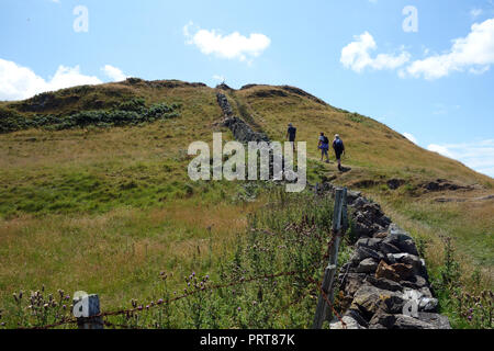 Ein Mann und zwei Frauen Wanderer vorbei Trockenmauer auf der Insel Anglesey Coastal Path in der Nähe des Fischerdorf Cemaes, Wales, UK. Stockfoto
