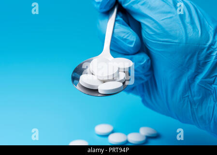 Arzt männliche Hand mit einem Löffel von Pillen Vitamine tabletten Drogen. Blauer Hintergrund mit weißen Pillen auf einer metallenen Löffel. Stockfoto