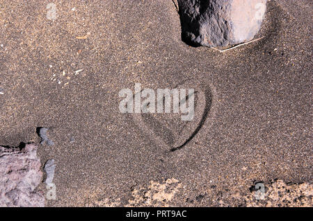 Das Symbol der Liebe auf dem schwarzen Sand in Form eines Herzens gezogen Stockfoto