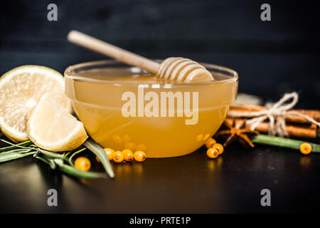 Die Zusammensetzung der Glasplatte mit Honig und Zitrone auf einem schwarzen Hintergrund ist das Konzept der ökologischen Lebensmittel und Gesundheit Stockfoto