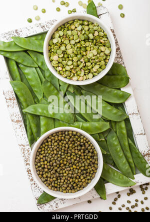 Schüssel mit Mungobohnen und Split peaswith organischen mangetout in Vintage hölzerne Kiste auf weiße Küche Hintergrund Stockfoto