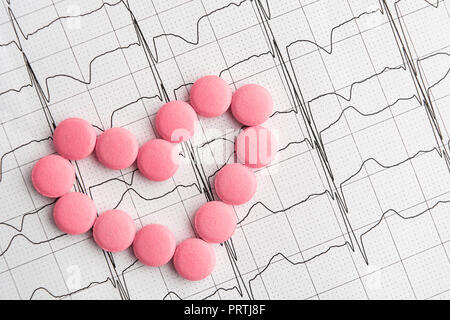 Pillen in Herzform über Papier Elektrokardiogramm, Ansicht von oben, flach Stockfoto