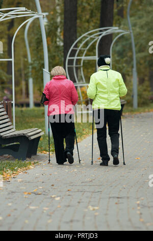 Reife Frauen tun Skandinavischen Wandern im Herbst im Park neben der Bank. Stockfoto