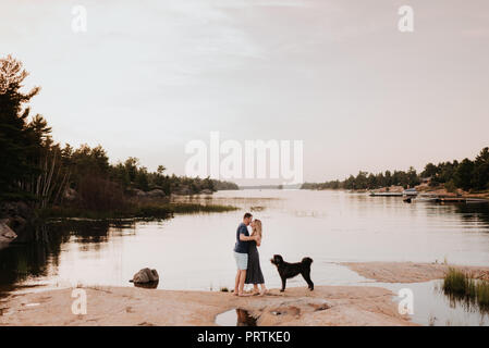 Paar beim Blick auf den Fluss mit Hund, Algonquin Park, Kanada Stockfoto