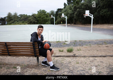 Männliche Teenager Basketball Spieler sitzen auf einer Parkbank, Basketballplatz, Porträt Stockfoto