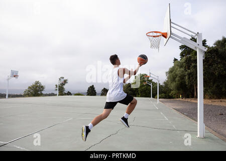 Männliche Teenager basketball Player springen mit Ball in Richtung Basketballkorb Stockfoto