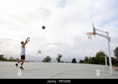 Männliche Jugendliche Basketballspieler wirft Ball in Richtung Basketballkorb Stockfoto