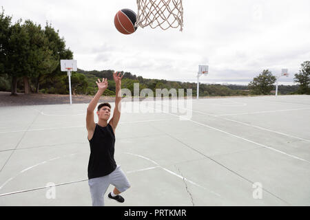 Männliche Jugendliche Basketballspieler wirft Ball in Richtung Basketballkorb Stockfoto