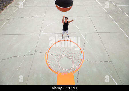 Männliche Jugendliche Basketballspieler wirft Ball in Richtung Basketballkorb, hohe Betrachtungswinkel Stockfoto