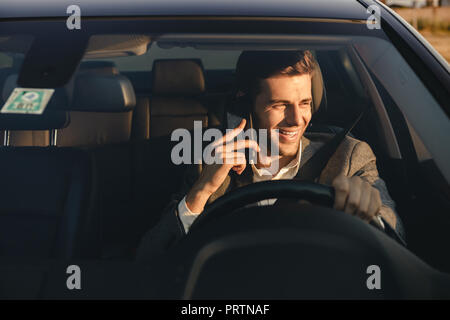 Vorderansicht des lächelnden bussinesman in seinem Auto fährt, Gespräch am Handy Stockfoto