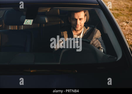 Vorderansicht des lächelnden bussinesman in seinem Auto fährt Stockfoto