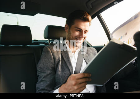 Gut aussehender Geschäftsmann durch Dokumente, während an der Rückseite eines Auto sitzen Stockfoto