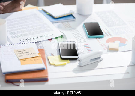 Smartphones mit Vertrag und Notebook mit Hefter auf Tisch im modernen Büro, Betriebsstätte Stockfoto