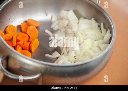 In Scheiben geschnittene orange Karotten und weißen Zwiebeln sind in Stahl Schale auf einem Küchentisch Stockfoto